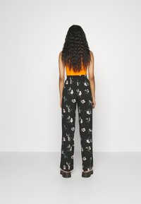 Czarne kwieciste spodnie o luźnym kroju, z zielonym i różowym wzorem kwiatów. Połączone z pomarańczowym topem bez rękawów.