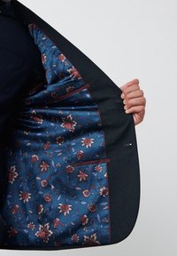Chaqueta de traje oscura hecha a medida con un forro azul con estampado floral que presenta acentos burdeos y múltiples bolsillos interiores.