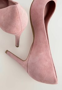 Vaaleanpunaiset mokkasiinit, joissa on terävä kärki ja stilettokanta. Käsittämätön pinta ja kaarevat reunat sekä tukeva vaaleanruskea pohja.