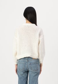 Chunky white knitted sweater with a rounded collar, oversized sleeves, and ribbed hem. Paired with light blue high-waisted denim jeans.