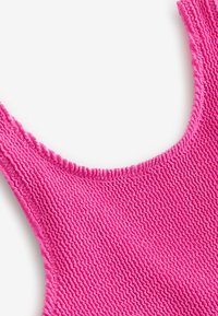 Tissu rose texturé avec un motif côtelé, présentant un large décolleté et des bretelles épaisses. Le matériau semble doux et souple.