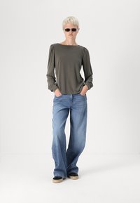 Olíva zöld, puffos vállú, hosszú ujjú felső, világoskék, bő szárú farmernadrággal párosítva, fekete, slip-on cipőkkel, bézs talppal.