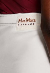 MaxMara Leisure witte stof tailleband met een getextureerd beige label waarop "MaxMara" in bruin is gedrukt, met gestikte details boven een effen gekleurd kledingstuk.