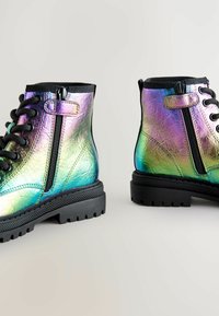 Bottines métalliques avec une finition holographique, featuring des lacets noirs, des fermetures éclair et des semelles en caoutchouc texturé pour une meilleure traction.
