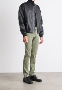 Svart läder bomberjacka med ribbade manchetter, dragkedja och quiltat mönster, kombinerad med olivgröna byxor och svarta snörskor.