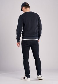 Mörkblå sweatshirt med rund halsringning, ribbade muddar och nederkant. I kombination med mörka jeans och vita sneakers med mörkblå detaljer.