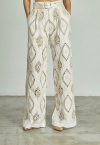 Pantaloni a gamba larga con una base bianca, adornati da motivi in pizzo beige, dotati di vita con cintura e tasche laterali.