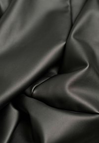 Schwarzer Kunstlederstoff mit einer glatten Textur, der sanfte Drapierungen und einen subtilen Glanz aufweist, und eine gleichmäßige Farbe ohne Muster zeigt.