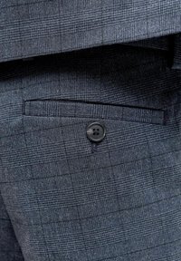 Sötétkék mintás szövet, kis kockás mintázattal. Oldalt egy tűrt zseb található, fekete gomb díszítéssel.