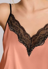 Satinowa koszulka w delikatnym odcieniu brzoskwini z subtelnym czarnym koronkowym wykończeniem wzdłuż dekoltu w kształcie litery V oraz cienkimi czarnymi ramiączkami. Gładka faktura, elegancki design.