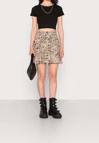 Černý žebrovaný crop top, vzorovaná béžová sukně s hnědými akcenty a černé chunky boty s detaily popruhů. Nosí texturovanou černou tašku.