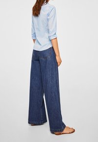 Camicia azzurra chiara a maniche lunghe con bottoni abbinata a jeans in denim blu scuro a gamba larga e morbida. I sandali hanno cinturini sottili. Design semplice e casual.