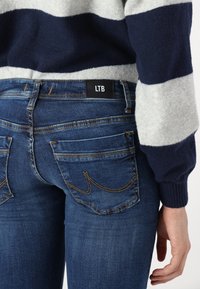 Jean en denim bleu foncé avec une texture lisse et une jambe fuselée, mettant en avant des coutures contrastées et une étiquette LTB sur la ceinture.