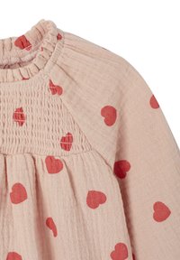 Helles rosa Bluse mit roten Herzmustern, mit einem gesmokten Oberteil und gerafftem Stoff. Der Ausschnitt hat einen Rüscheneinsatz.