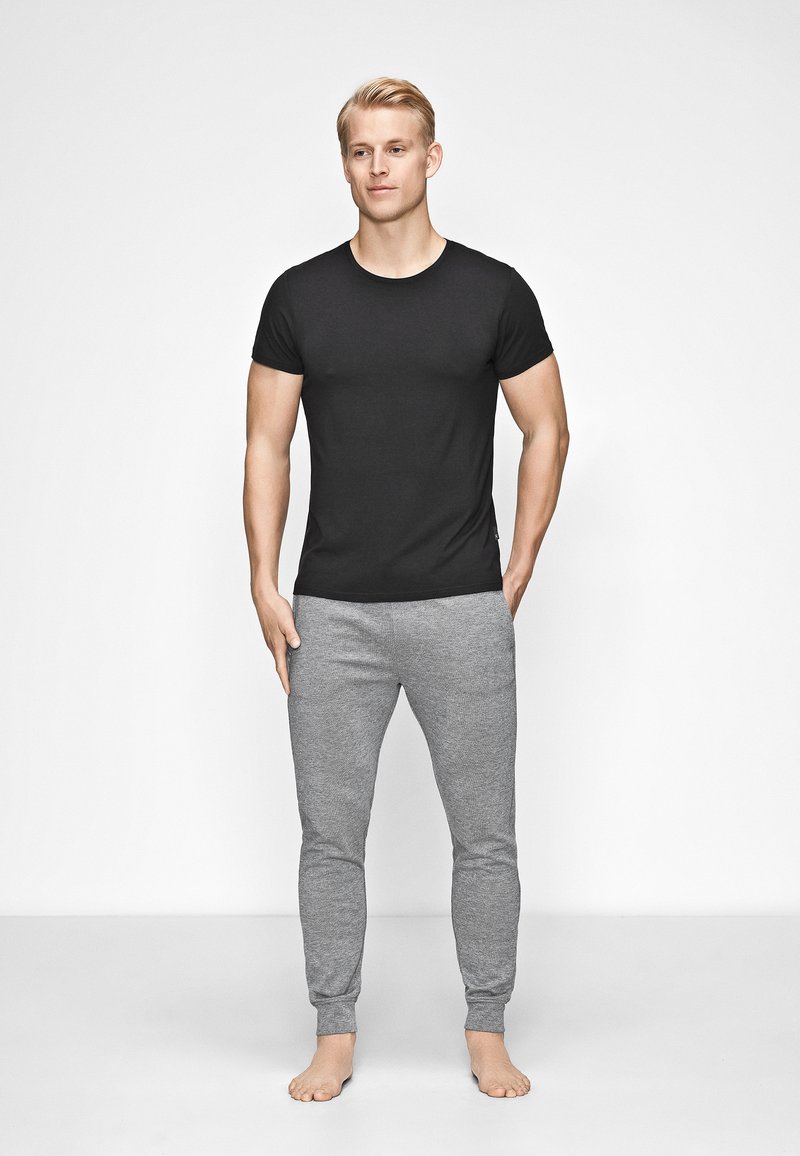 Sort tætsiddende T-shirt og grå tapered sweatpants. T-shirten har korte ærmer, mens bukserne har en blød tekstur og manchetter ved anklerne.