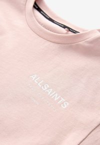 Světle růžové bavlněné tričko s kulatým výstřihem, zdobené bílým potiskem "ALLSAINTS LONDON" a japonskými znaky pod ním. Měkká textura.