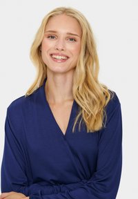 Blusa avvolgente marina con maniche lunghe, texture morbida e scollatura a V. Presenta linee semplici e un fit rilassato per il massimo comfort.