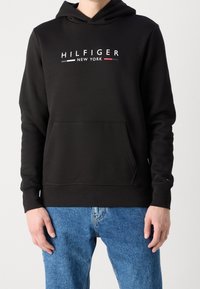 Felpa con cappuccio nera in cotone con tasca frontale, caratterizzata da un logo "HILFIGER NEW YORK" con accenti bianchi e rossi.