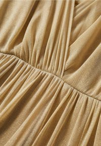 Un tissu de couleur or avec un léger éclat, présentant des plis froncés et une texture douce, crée des rides fluides qui mettent en valeur son design.
