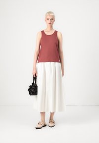 Bordový top bez rukávů s kulatým výstřihem, zkombinovaný s bílou volnou maxi sukni. Modelka drží černou texturovanou kabelku a má na sobě béžové plátěné boty.