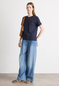Námornícky bavlnený tričko s jemne vyšitým logom, kombinované so svetlo modrými širokými džínsy a šedými teniskami. Hnedá crossbody taška.