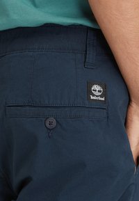 Navyblauwe katoenen shorts met een achterzak met een zwart Timberland-logo patch en knoopsluiting. Gladde textuur, op maat gemaakte ontwerp.