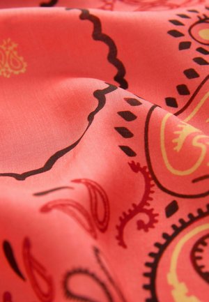 Közeli kép piros anyagról, melynek fekete és sárga paisley mintái vannak, valamint redők árnyék- és fényhatásokat hoznak létre.