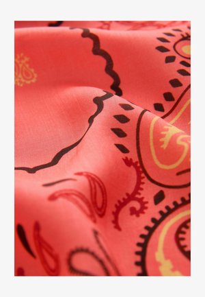 Közeli kép piros anyagról, melynek fekete és sárga paisley mintái vannak, valamint redők árnyék- és fényhatásokat hoznak létre.