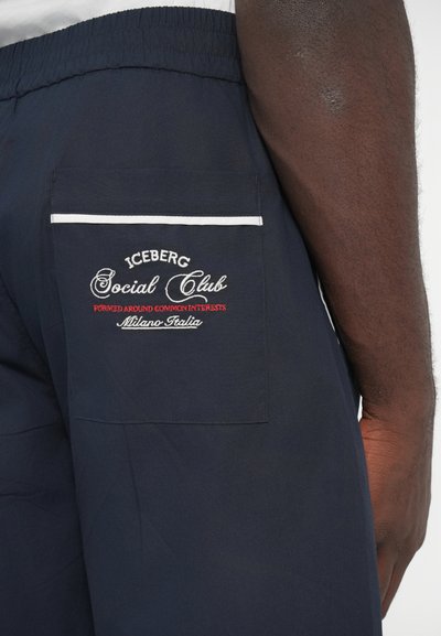 Σορτς σε ναυτικό μπλε με ελαστική μέση, διαθέτουν πίσω τσέπη διακοσμημένη με κόκκινο και λευκό κεντητό κείμενο "Iceberg Social Club" και λευκή επένδυση.