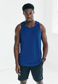 Granatowy tank top męski wykonany z tkaniny odprowadzającej wilgoć, z okrągłym dekoltem i kontrastowymi szwami, zestawiony z czarnymi szortami.