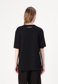 Black t-shirt with short sleeves and a relaxed fit. Features a crew neckline and a white logo text at the back near the collar.