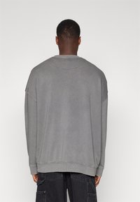 Sudadera gris de gran tamaño con cuello redondo acanalado, hombros caídos y tejido ligeramente texturizado. El dobladillo y los puños presentan detalles de costura.