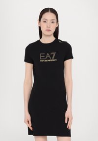 Μαύρο φόρεμα κοντό μανίκι από ελαστικό ύφασμα, με εκτύπωση χρυσού λογότυπου και διακριτές λεπτομέρειες στους ώμους. Στενή γραμμή.