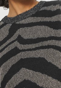 Pull rayé noir et argent avec un tricot texturé, comprenant un fil métallique au niveau du col et un motif en zigzag sur le tissu.