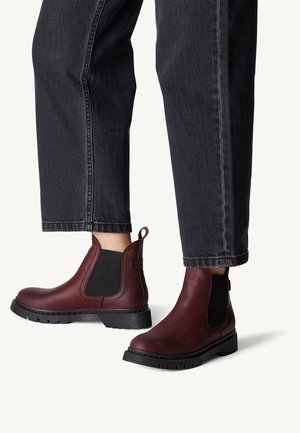Bottines en cuir bordeaux avec des côtés en élastique noir, bout rond, petit talon carré et semelle en caoutchouc texturée. Jean avec un ourlet cropped visible.
