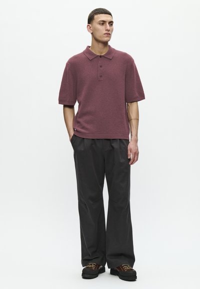 Polo de culoare burgundă, cu mânecă scurtă, din țesătură texturată, cu un guler cu trei nasturi, asociat cu pantaloni largi de culoare gri închis și încălțăminte solidă de culoare neagră.