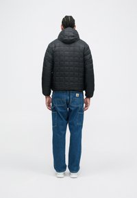 Black quilted puffer jacket with a hood, featuring a cropped cut and boxy shape. Worn with blue denim pants and white sneakers.