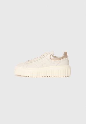 Sneaker crema a bassa altezza con suola spessa e scanalata, allacciatura frontale e accentuazione metallica dorata sul colletto del tallone, mostrata in profilo laterale.