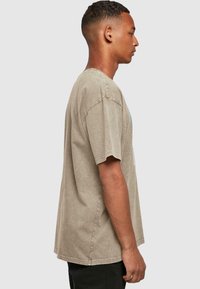 Lysbrun bomulds tshirt med korte ærmer, afslappet pasform, rund halsudskæring og subtil tekstur. Har et grafisk print i turkis.