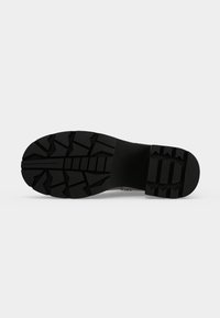 Semelle de botte en caoutchouc noir avec des motifs de bande de roulement profonds et anguleux pour une bonne adhérence sur un fond clair uni.