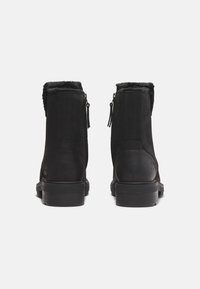 Botine negre cu căptușeală din blană, închidere cu fermoar și panouri texturate. Fabricate din suede și piele, având o talpă robustă din cauciuc.