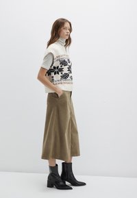 Knit sweater vest with floral pattern, cream and black colors; paired with olive corduroy wide-leg pants and black ankle boots.