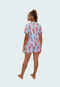 Pijamas cortos con estampado de langostas en tela azul claro, con puños a rayas negras y blancas. Modelo mostrado de espaldas, descalzo.