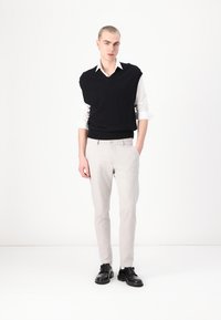 Zwarte gebreide vest over een wit shirt, gecombineerd met lichtgrijze broek en zwarte schoenen. De outfit heeft een v-hals en een recht gesneden ontwerp.