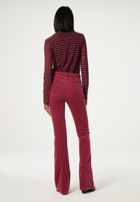 Langärmliges Shirt mit einem schwarz-roten Herzmuster, kombiniert mit burgunderroten, ausgestellten Cordhosen mit einem taillierten Bund und Gesäßtaschen.