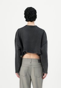 Felpa grigia a maniche lunghe con collo rotondo, spalle scese e polsini a costine; abbinata a pantaloni grigi chiari con tasche posteriori.