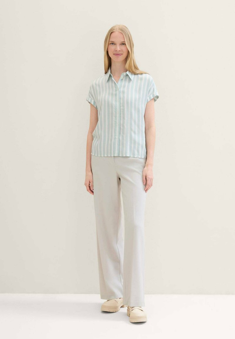 Light blue and white striped short-sleeve shirt with button closure, paired with light gray trousers and chunky beige shoes.
