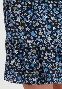 Vestido floral con fondo negro, adornado con flores azules, blancas y verdes. Tejido suave, con un dobladillo con volantes en capas para mayor textura.