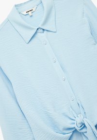 Lichtblauwe button-up shirt van gestructureerde stof, met een kraag, zes witte knopen en een strikdetail bij de taille.