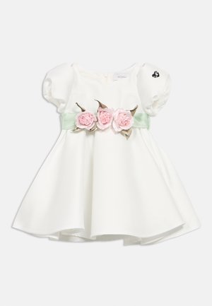 Biała sukienka dla niemowląt z bufkami na rękawach, zielonym paskiem wokół talii i trzema różowymi kwiatami z tkaniny na środku.